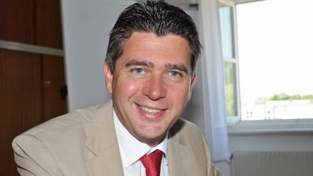 Ein lächelnder Mann in einem hellen Anzug und roter Krawatte.