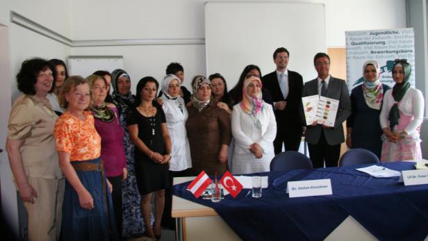 Eine Gruppe von Frauen und Männern posiert für ein Foto vor einem Tisch mit österreichischen und türkischen Flaggen.