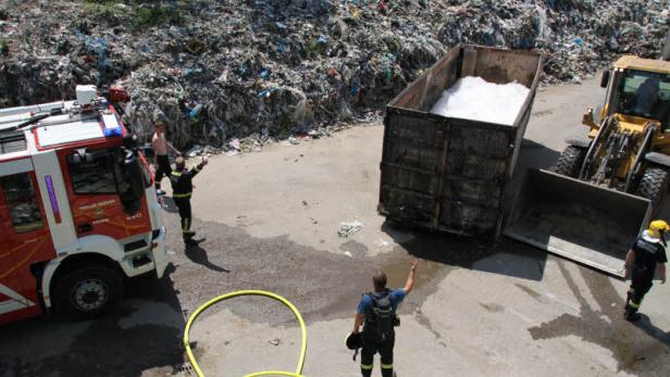 Feuerwehrleute inspizieren einen Müllberg und einen mit Schaum gefüllten Container.