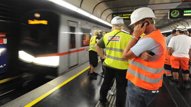 Bauarbeiter in Warnwesten stehen an einem Bahnsteig, während eine U-Bahn vorbeifährt.