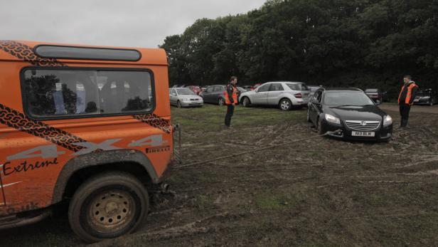 Ein orangefarbener Geländewagen zieht ein schwarzes Auto aus dem Schlamm.