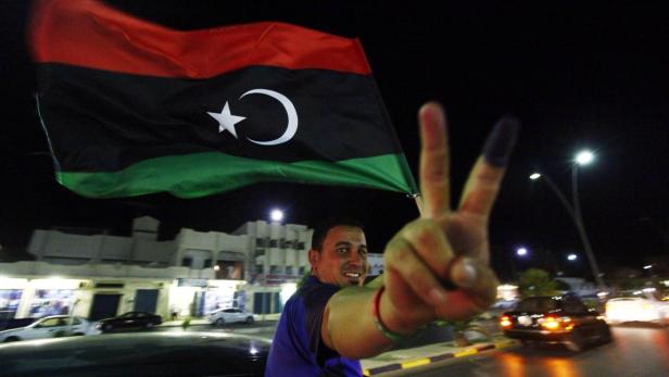 Ein Mann hält eine libysche Flagge und zeigt ein Siegeszeichen.