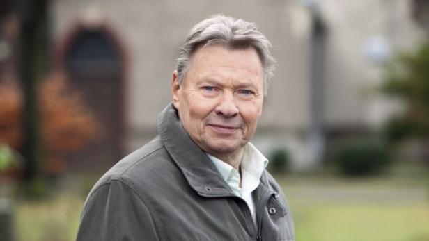 Ein älterer Mann mit grauen Haaren und einer grauen Jacke blickt in die Kamera.