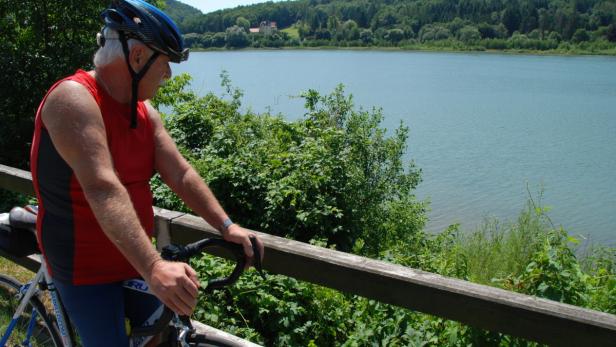 Ein Radfahrer mit Helm macht eine Pause mit Blick auf einen See.