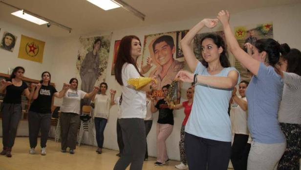 Eine Gruppe Frauen tanzt in einem Raum mit politischen Postern an den Wänden.