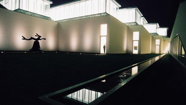 Ein moderner Museumsbau mit einer Hasenstatue im Hof bei Nacht.