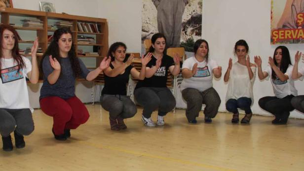 Eine Gruppe junger Frauen hockt auf dem Boden und klatscht in die Hände.