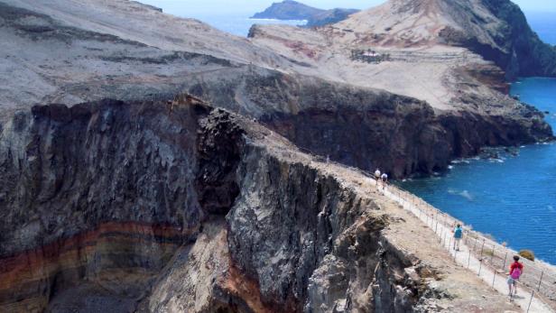 Wanderer auf einem schmalen Pfad entlang einer Klippe mit Blick auf das Meer.