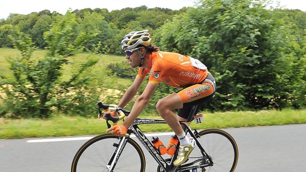 Ein Radfahrer in orangefarbener Teamkleidung fährt auf einer Landstraße.