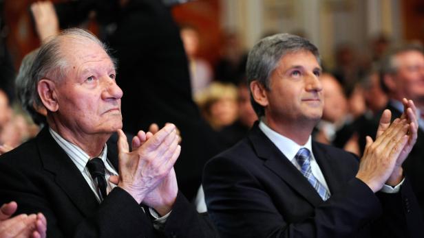 Zwei Männer in Anzügen applaudieren bei einer Veranstaltung.