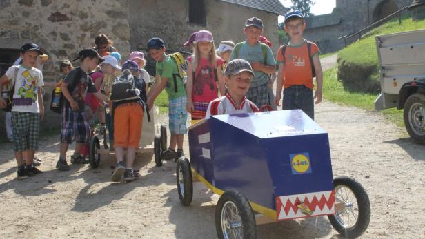 Eine Gruppe Kinder steht um ein blaues Seifenkistenfahrzeug mit Lidl-Logo.
