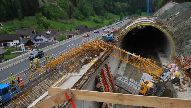 Eine Baustelle an einem Tunnel mit Bauarbeitern und einem Kran.
