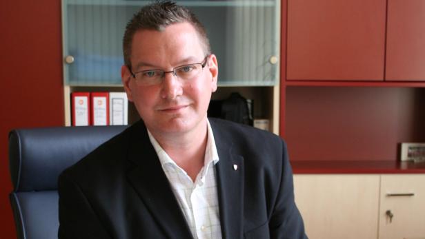 Ein Mann mit Brille und Anzug sitzt in einem Büro.