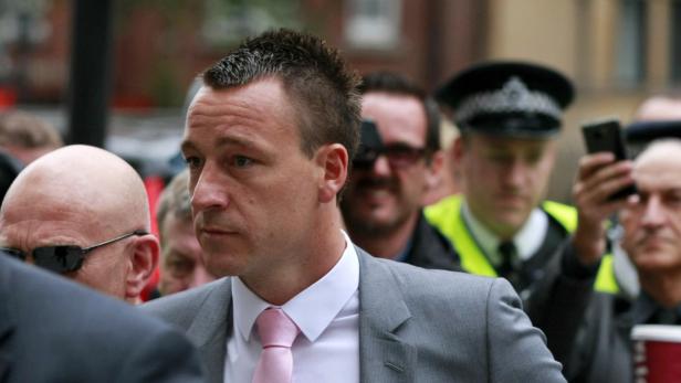 Ein Mann in einem grauen Anzug und rosa Krawatte inmitten einer Menschenmenge.