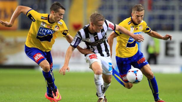 Drei Fußballspieler kämpfen um den Ball auf dem Spielfeld.