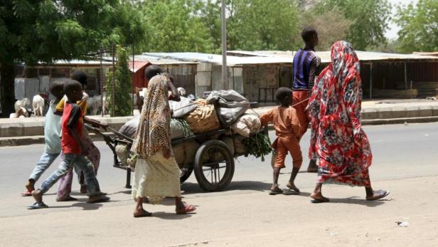 Eine Gruppe von Menschen zieht einen Karren mit Waren über eine Straße.