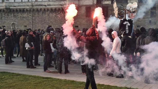 Eine Menschenmenge demonstriert mit Rauch und Fackeln in einer städtischen Umgebung.