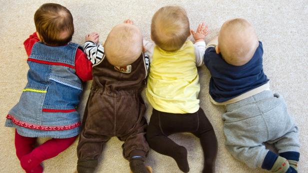 Vier Babys liegen nebeneinander auf dem Bauch auf einem Teppich.