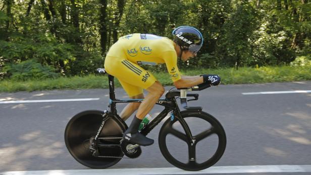 Ein Radfahrer im gelben Trikot fährt ein Zeitfahrrad auf einer asphaltierten Straße.