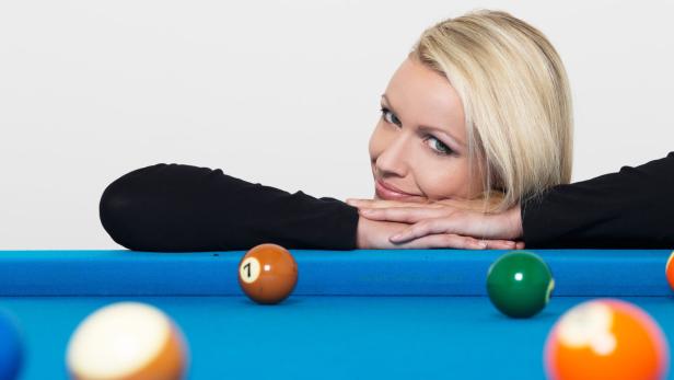 Eine blonde Frau lehnt auf einem Billardtisch mit Billardkugeln.