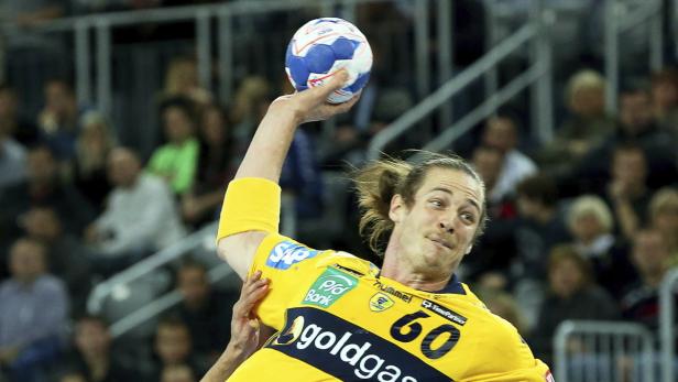 Ein Handballspieler in gelbem Trikot wirft einen Ball vor einer Zuschauermenge.