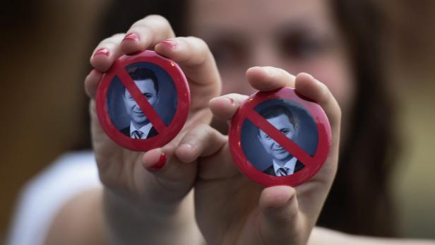 Eine Frau hält zwei Buttons mit durchgestrichenen Porträts von Baschar al-Assad hoch.