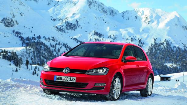 Ein roter VW Golf steht im Schnee vor einer verschneiten Berglandschaft.