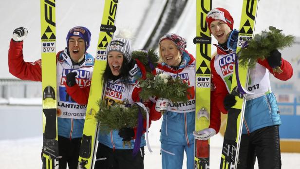 Vier Skispringer stehen mit Skiern und Blumensträußen auf dem Siegerpodest.