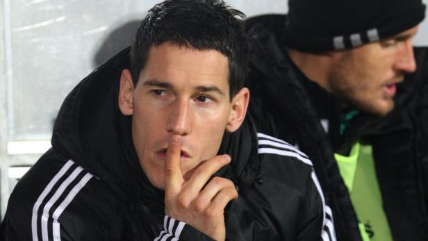 Ein Mann in einer schwarzen Jacke hält den Finger vor den Mund.