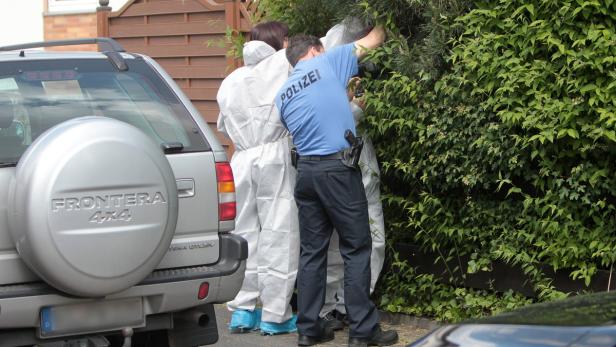 Polizisten suchen in Schutzanzügen in einem Gebüsch nach Spuren.