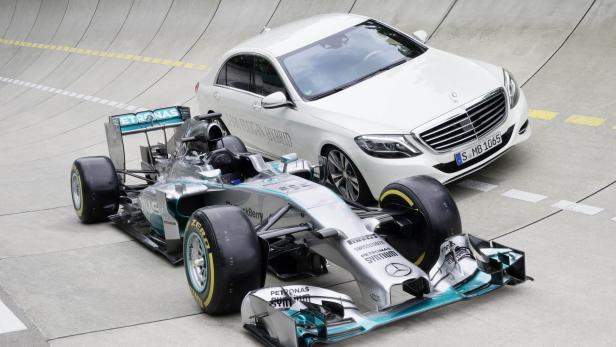 Ein Formel-1-Rennwagen und eine weiße Mercedes-Benz S-Klasse auf einer Rennstrecke.