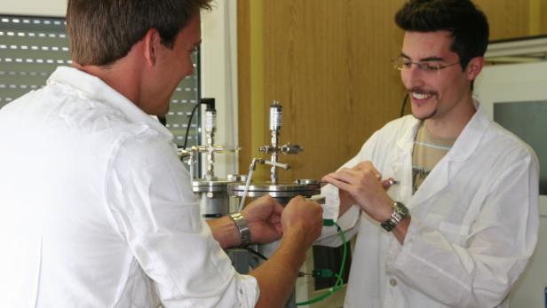 Zwei Männer in Laborkitteln arbeiten an einer wissenschaftlichen Apparatur.