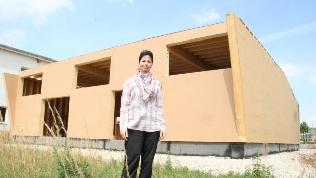 Eine Frau steht vor einem im Bau befindlichen Holzhaus.