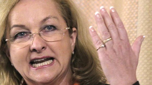 Eine Frau mit Brille gestikuliert mit ihrer Hand, an der sie mehrere Ringe trägt.