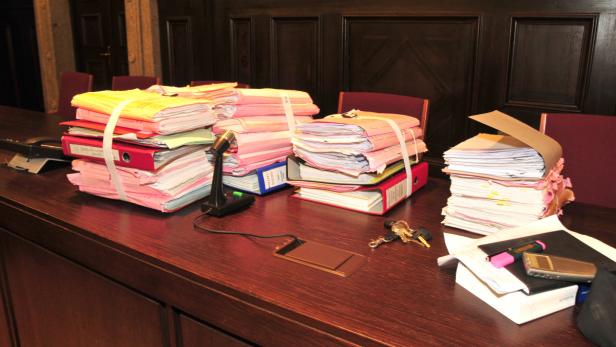 Ein Schreibtisch ist mit Aktenordnern, Dokumenten und Büroartikeln bedeckt.