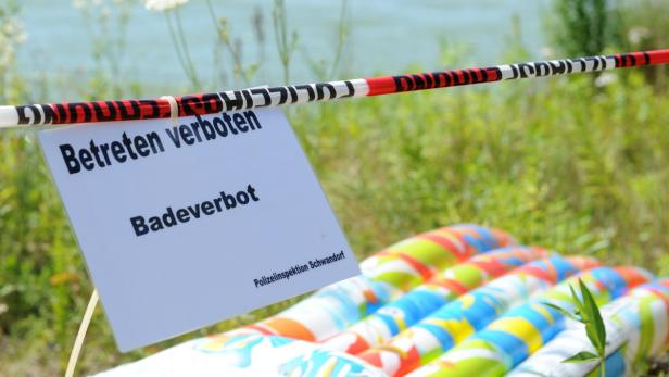 Ein Schild mit der Aufschrift „Betreten verboten“ und „Badeverbot“ vor einer Wiese.