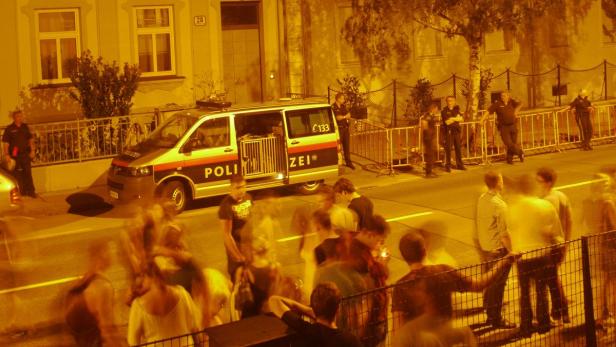 Eine Menschenmenge steht vor einem Polizeiwagen auf der Straße.