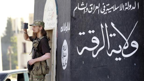 Ein europäischer Söldner vor einem Haus mit IS-Symbolen.