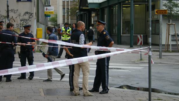 Polizisten stehen auf der Straße, die mit rot-weißem Flatterband abgesperrt ist.