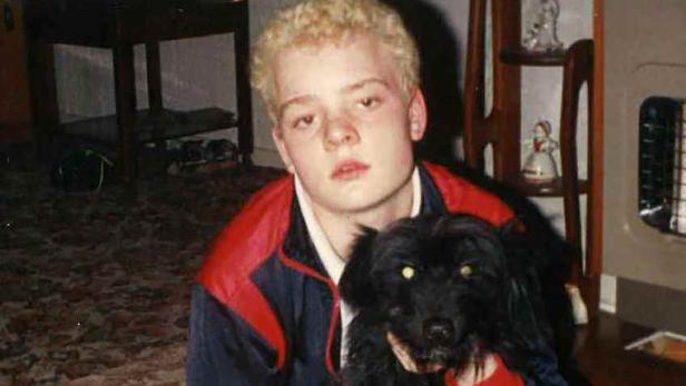 Ein junger Mann mit blonden Haaren posiert mit einem schwarzen Hund.