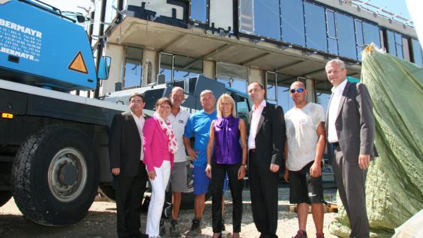 Eine Gruppe von Personen steht vor einem Gebäude mit einem Kranwagen der Firma Bermayr.