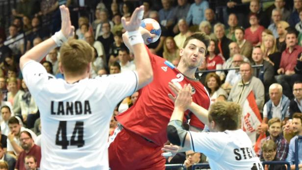 Ein Handballspieler in rotem Trikot wirft den Ball während eines Spiels.