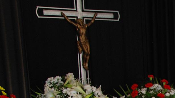 Ein Kruzifix mit Blumen vor einem schwarzen Hintergrund.