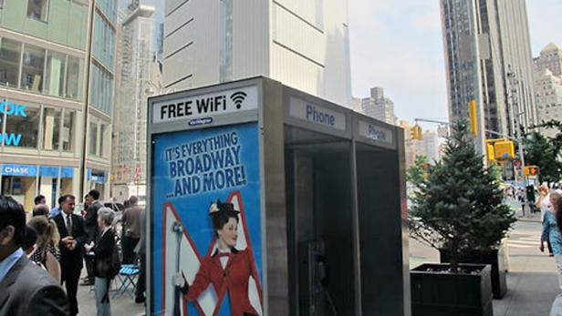 Eine Telefonzelle mit Werbung für kostenloses WLAN und Broadway-Shows in einer belebten Stadt.