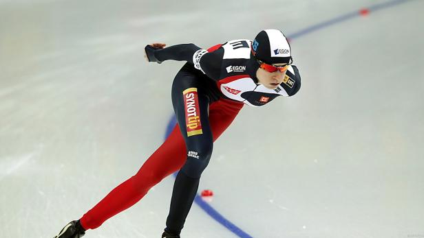 Eine Eisschnellläuferin in rot-schwarzer Rennausrüstung auf dem Eis.