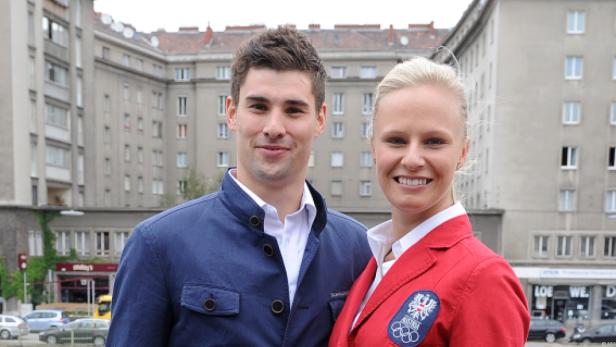 Ein Mann und eine Frau in Sportjacken posieren vor einem Gebäude.