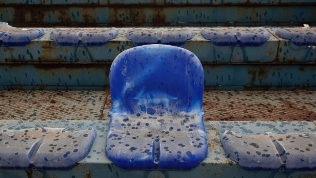 Eine Reihe abgenutzter, blauer Stadionsitze.