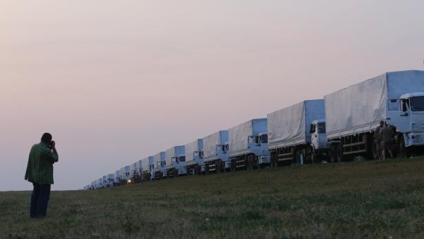 Ein Mann telefoniert vor einer langen Reihe parkender Lastwagen.