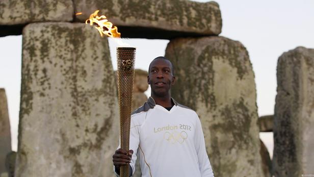 Ein Mann hält die olympische Fackel vor Stonehenge.