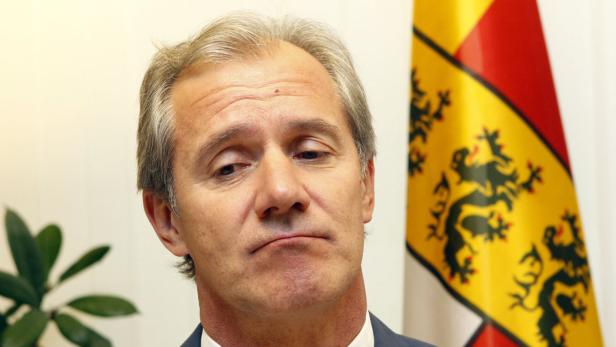 Ein Mann mit grauem Haar steht vor einer Flagge mit einem schwarzen Löwen.